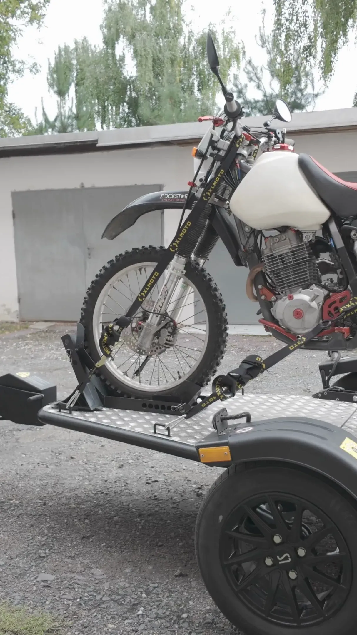 Motorrad auf einem PKW-Anhänger, angekuppelt an einen silbernen Kastenwagen